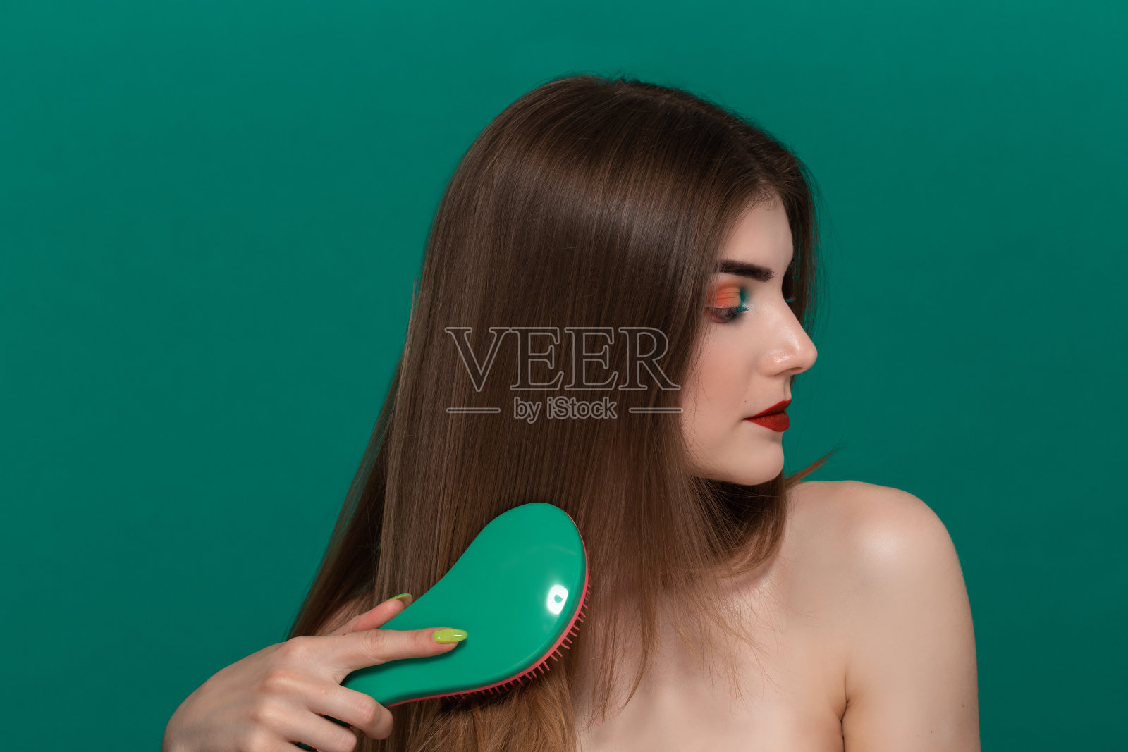 美丽的年轻女子肖像与明亮的颜色化妆梳头发与绿色刷照片摄影图片