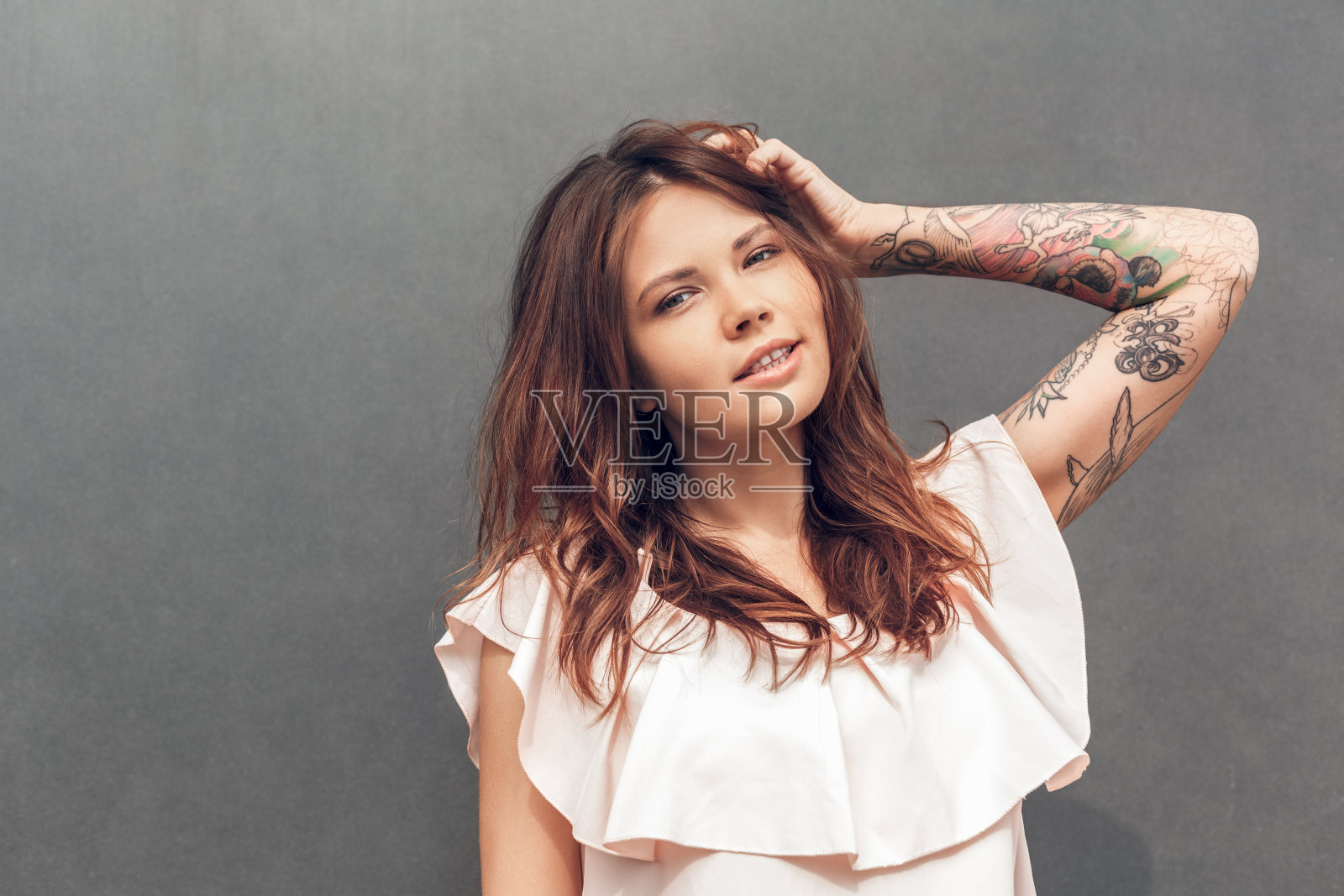 自由泳。女孩孤立地站在灰色的城市街道上，对着相机摆姿势，触摸头发，微笑，性感照片摄影图片