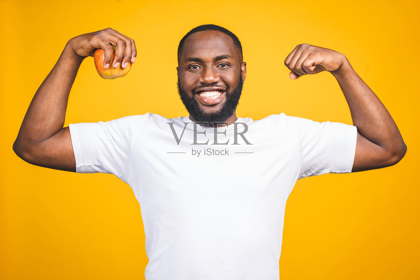 健康的非裔美国人拿着一个苹果孤立的黄色背景。照片摄影图片