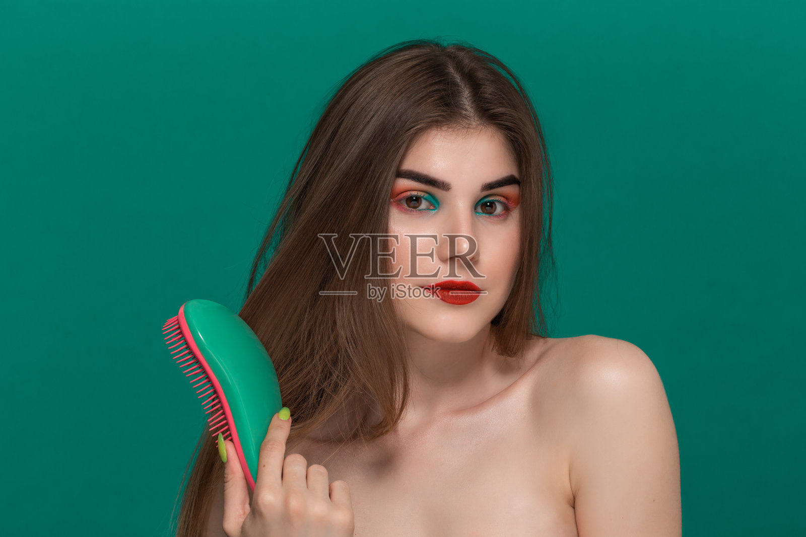 美丽的年轻女子肖像与明亮的颜色化妆梳头发与绿色刷照片摄影图片