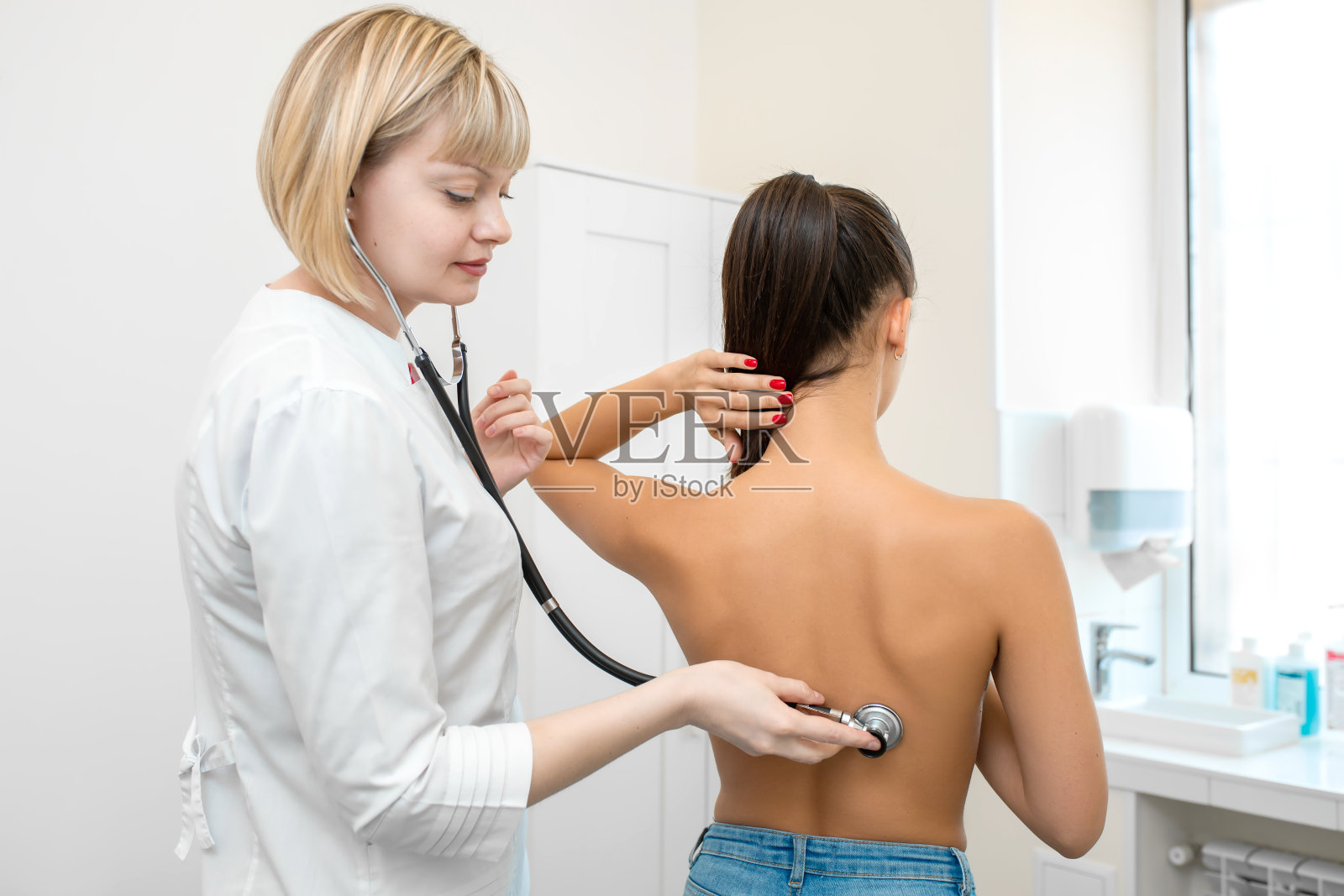 女医生治疗师用听诊器听一个年轻的女性病人照片摄影图片