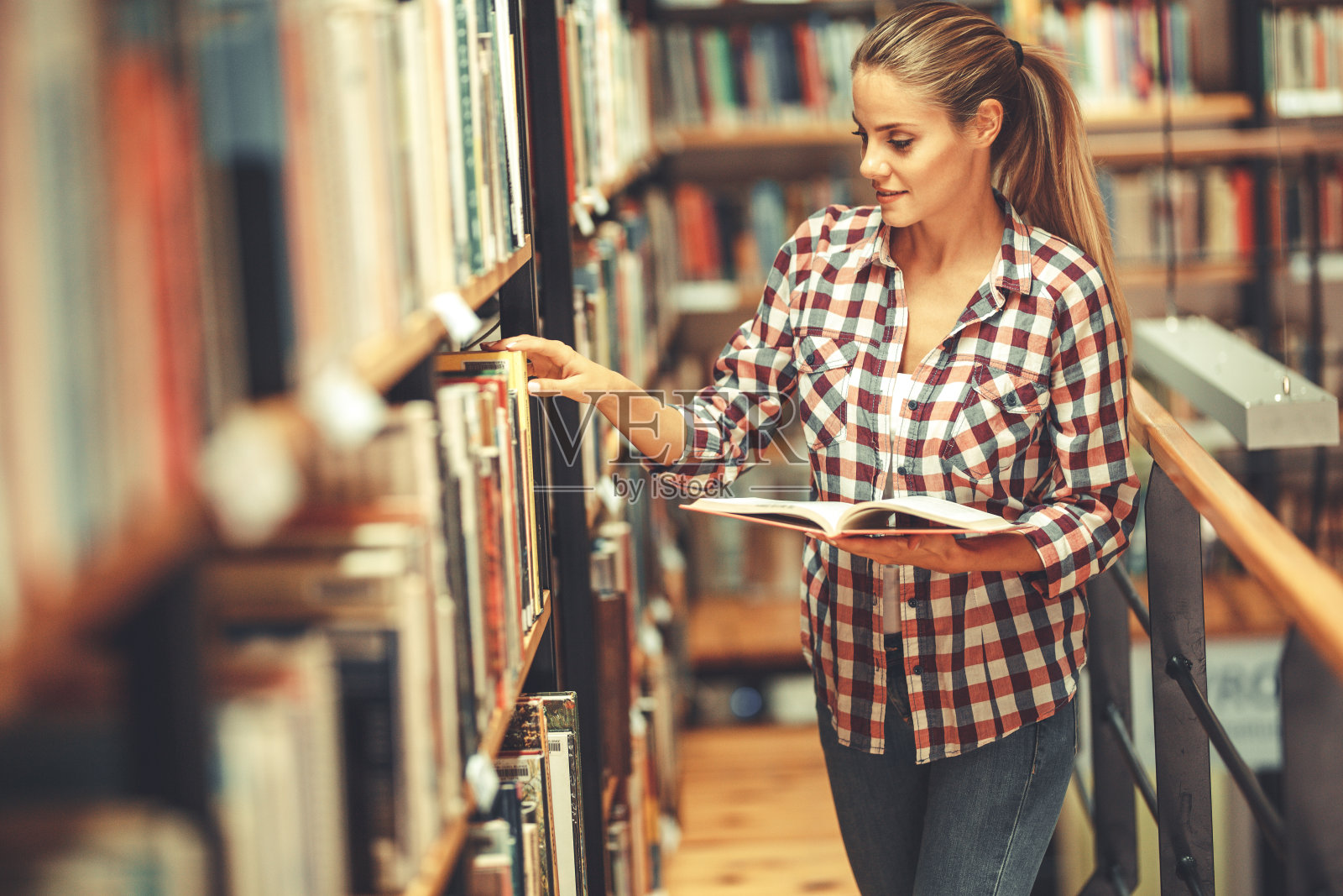 年轻女学生在图书馆的书架上阅读和学习。照片摄影图片