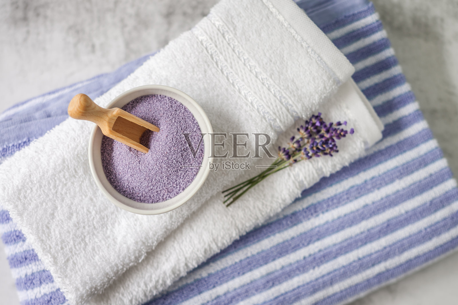 一堆干净的软毛巾和一堆薰衣草和浴盐在浅灰色的背景。照片摄影图片