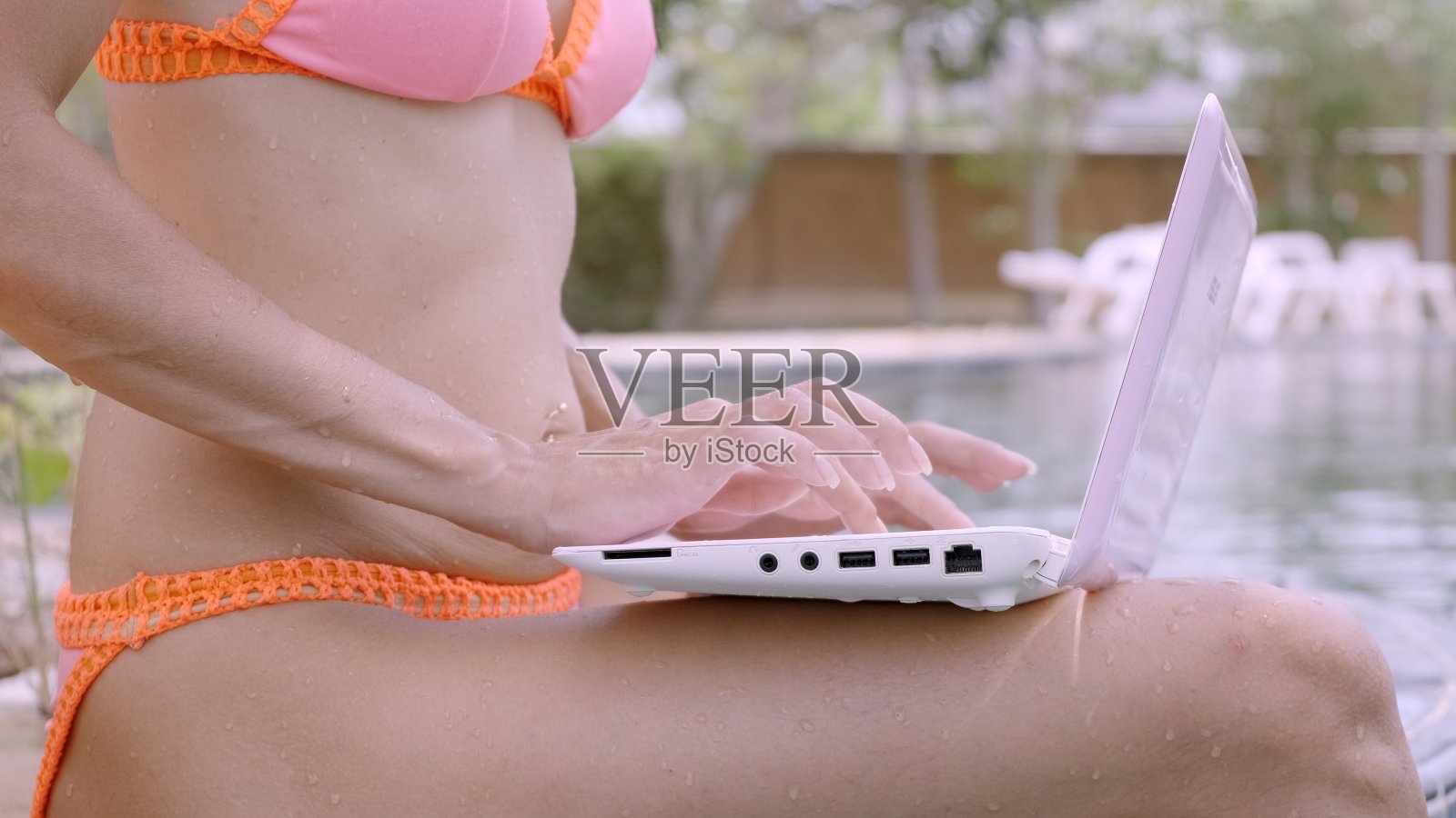 年轻女性自由职业者，在泳池边拿着笔记本电脑。假期很忙。远程工作的概念。特写镜头照片摄影图片