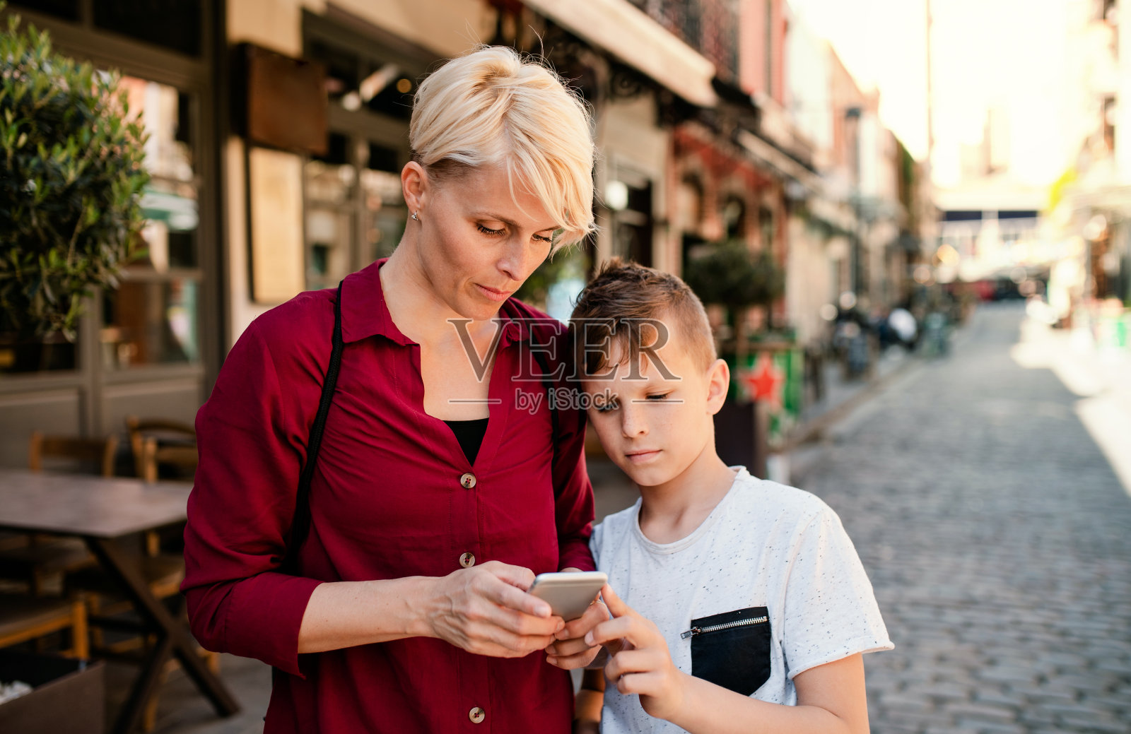 母亲和儿子站在地中海小镇的户外，使用智能手机。照片摄影图片