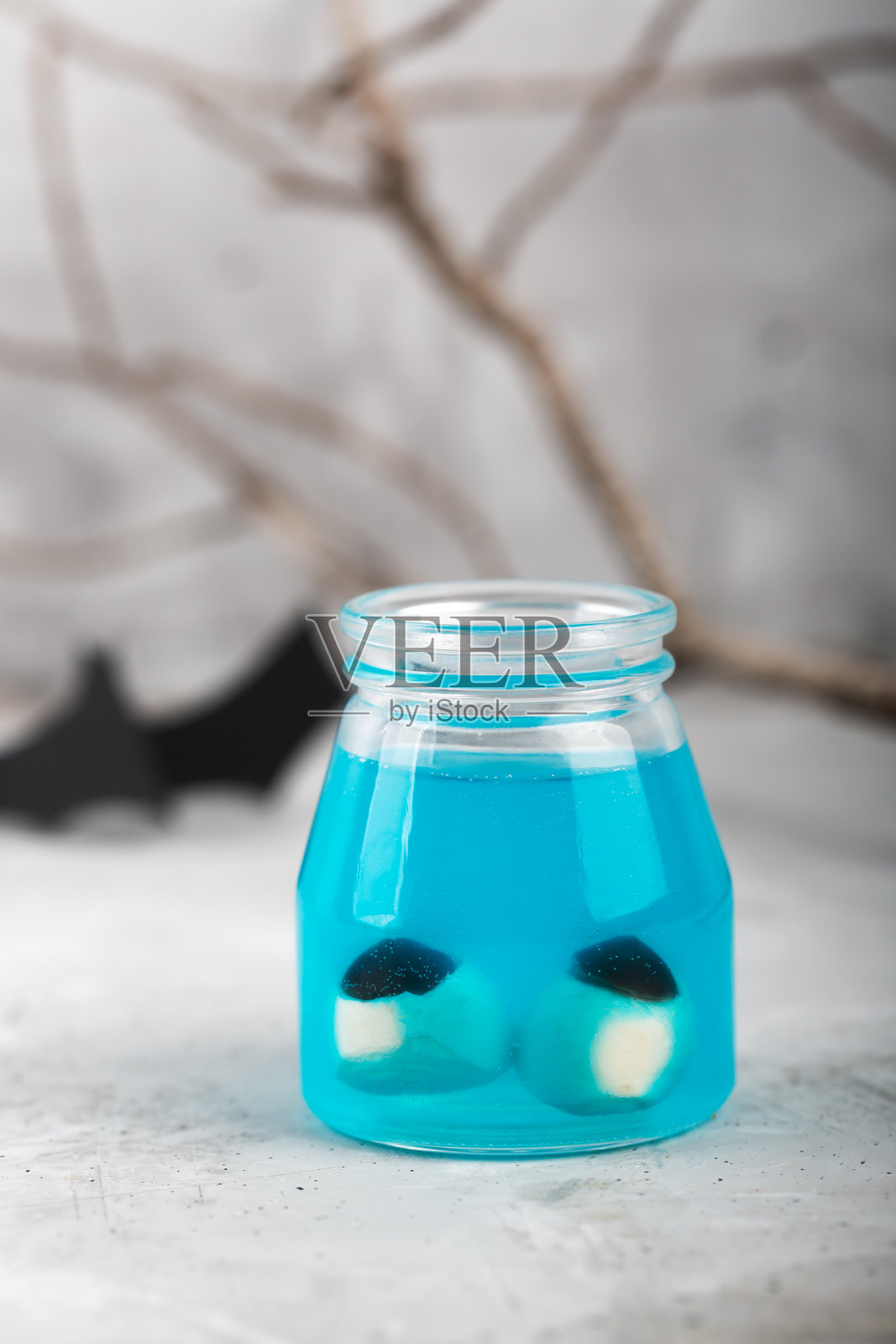 万圣节的概念——在灰色背景下，蓝色液体里装着两只假眼睛照片摄影图片