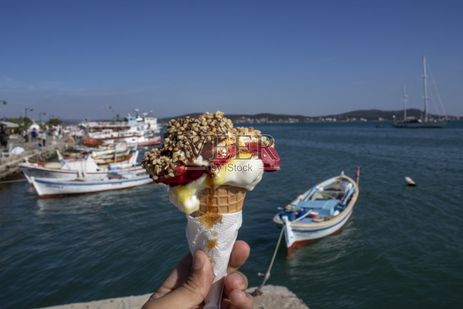 手握冰淇淋。背景是大海，天空和船只照片摄影图片