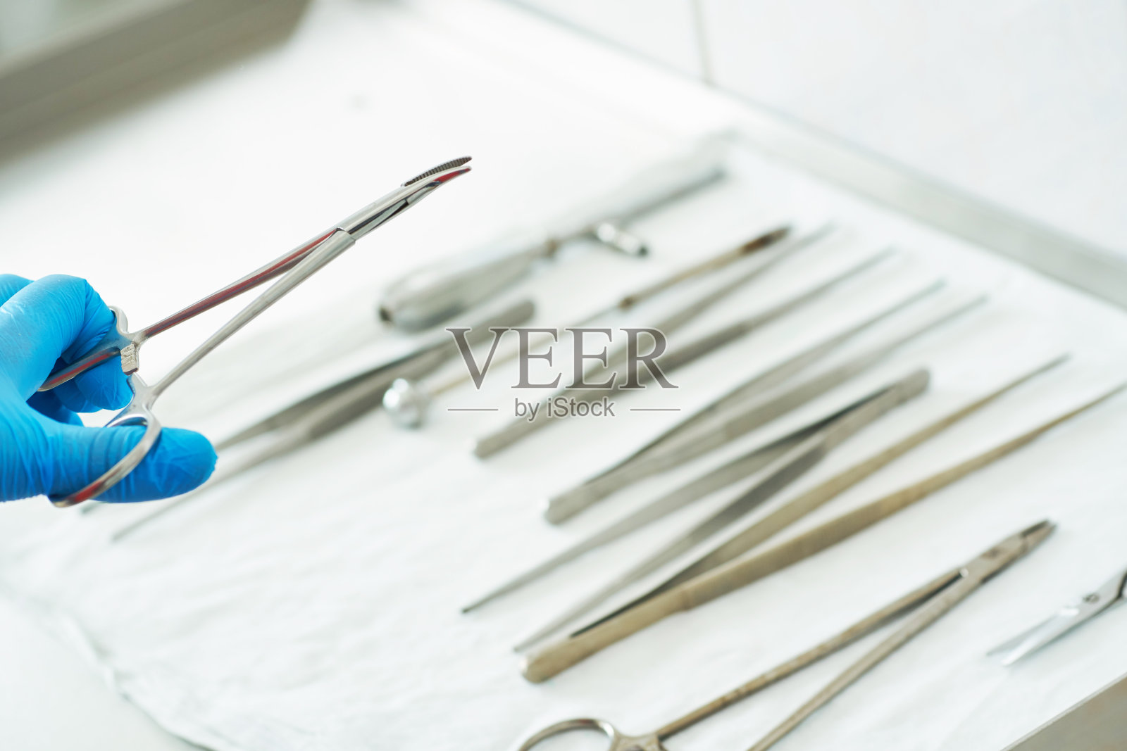 一个戴着蓝色医用手套的护士的手拿着夹子。手术用的医疗器械放在背景手术室的金属桌子上。照片摄影图片