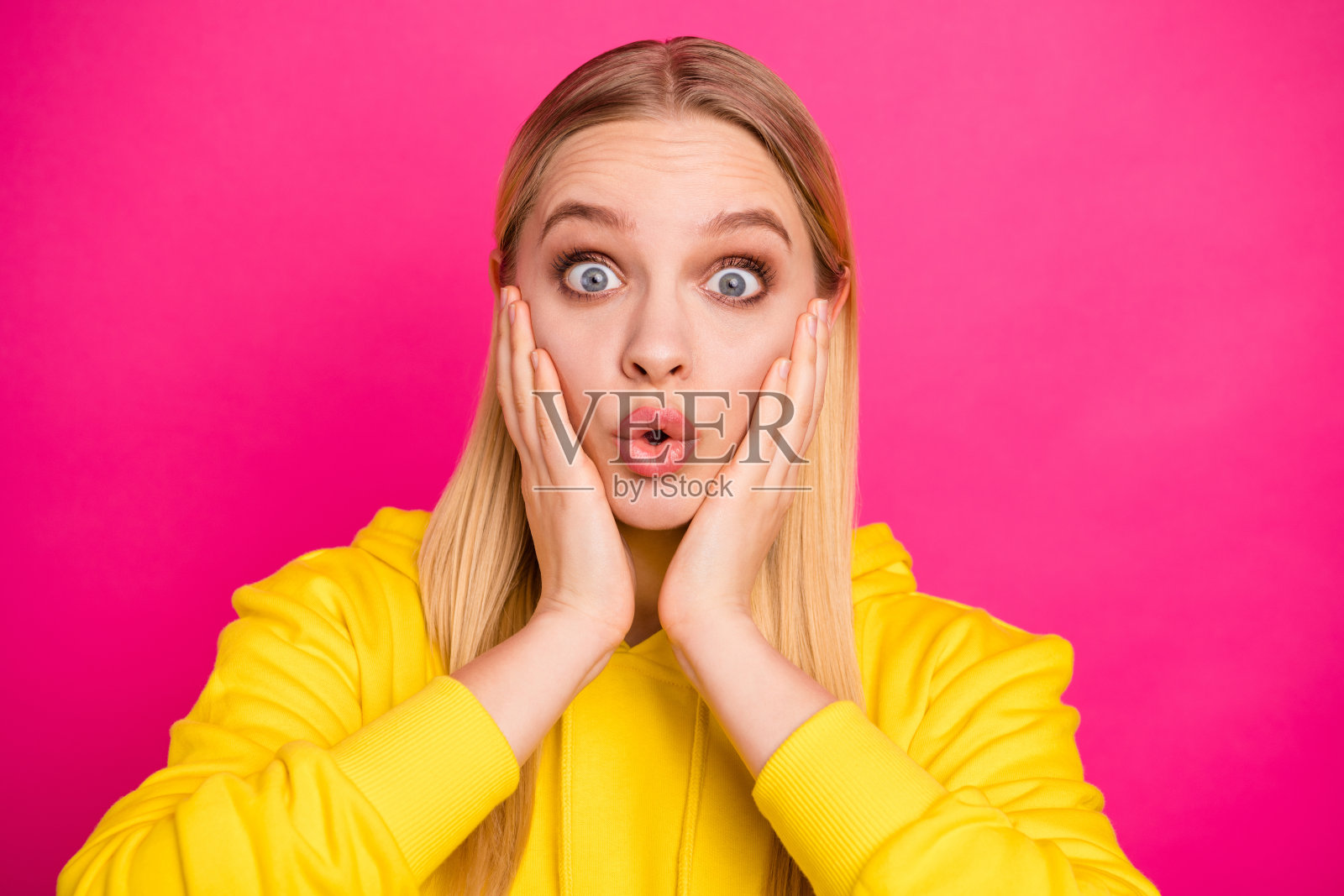 照片上的女士不相信可怕的新闻双手在颧骨上穿黄色连帽衫孤立的粉色背景照片摄影图片