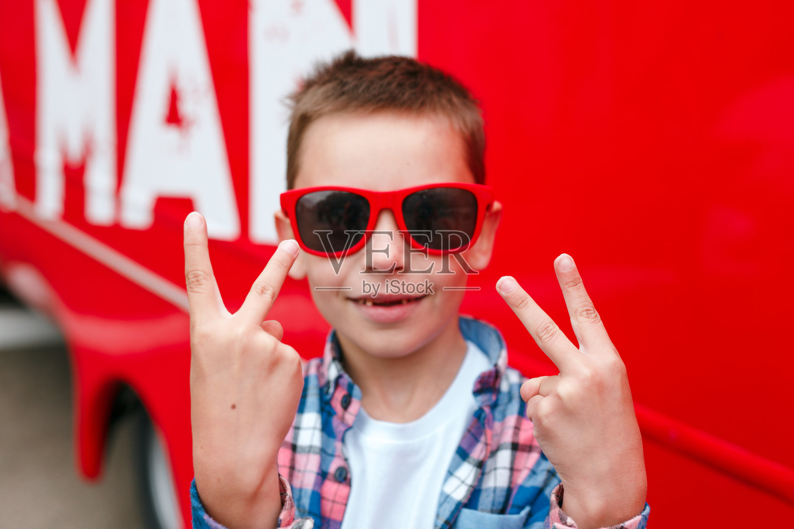 戴着红色太阳镜的时尚小男孩在户外展示和平标志照片摄影图片