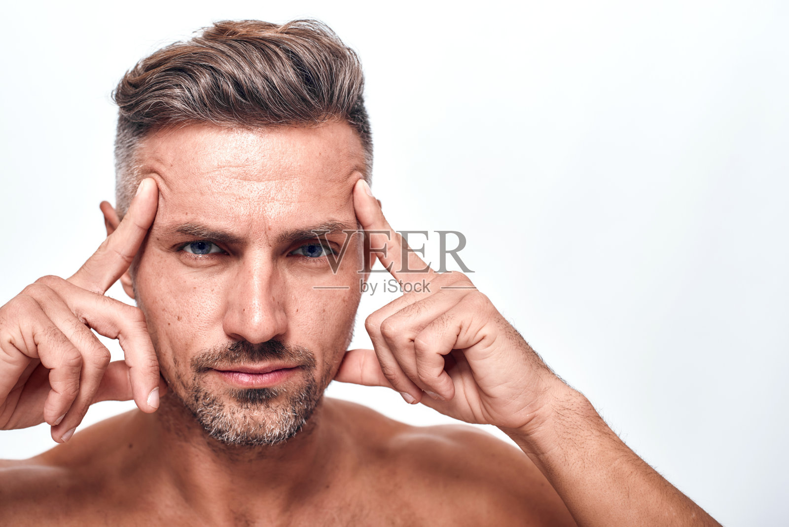 男性美。帅气和性感的男人，留胡子的手拿着头，看着镜头，而站在灰色的背景照片摄影图片