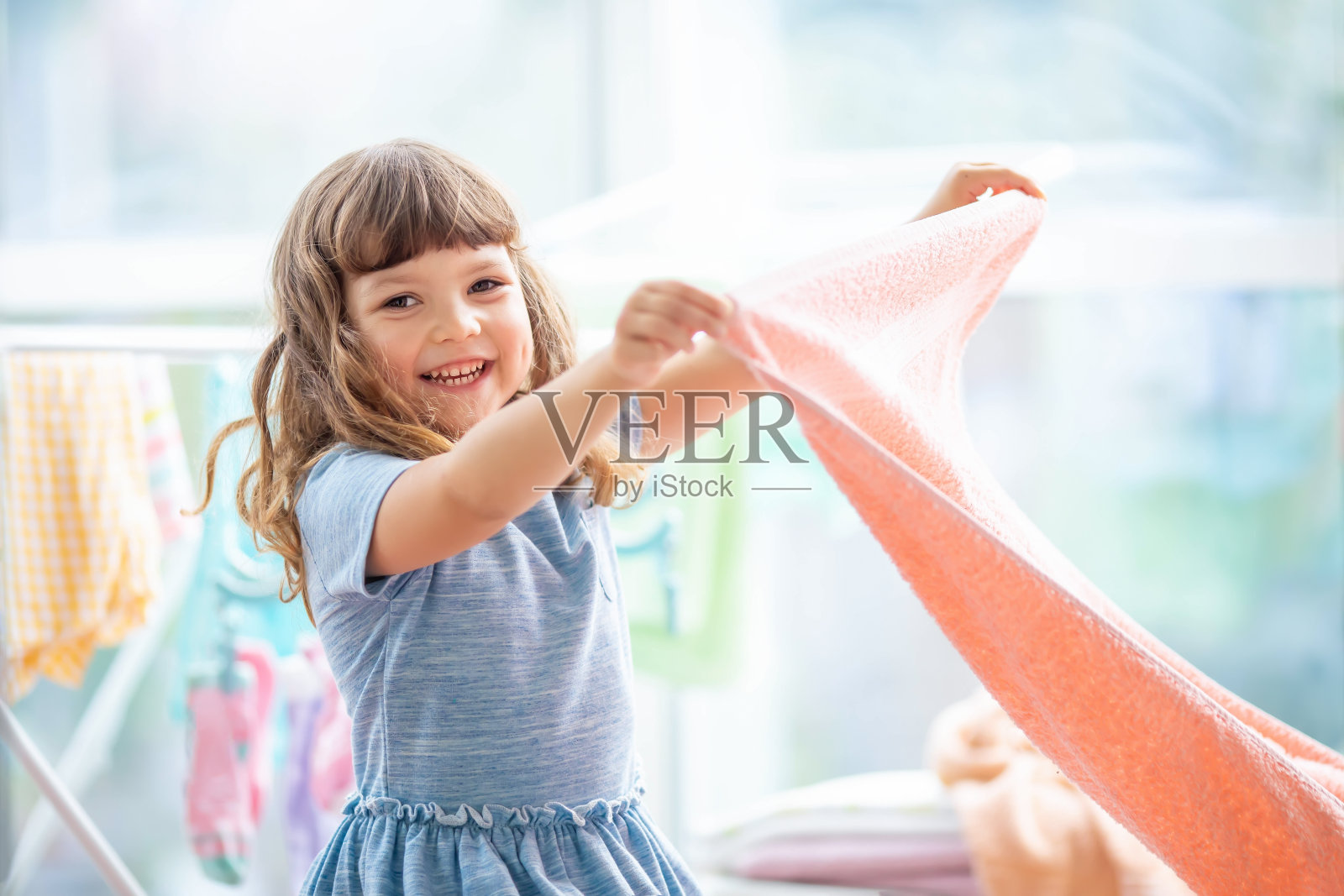 孩子在洗衣房。洗干净的衣服放在晾衣架上。妈妈的小助手照片摄影图片