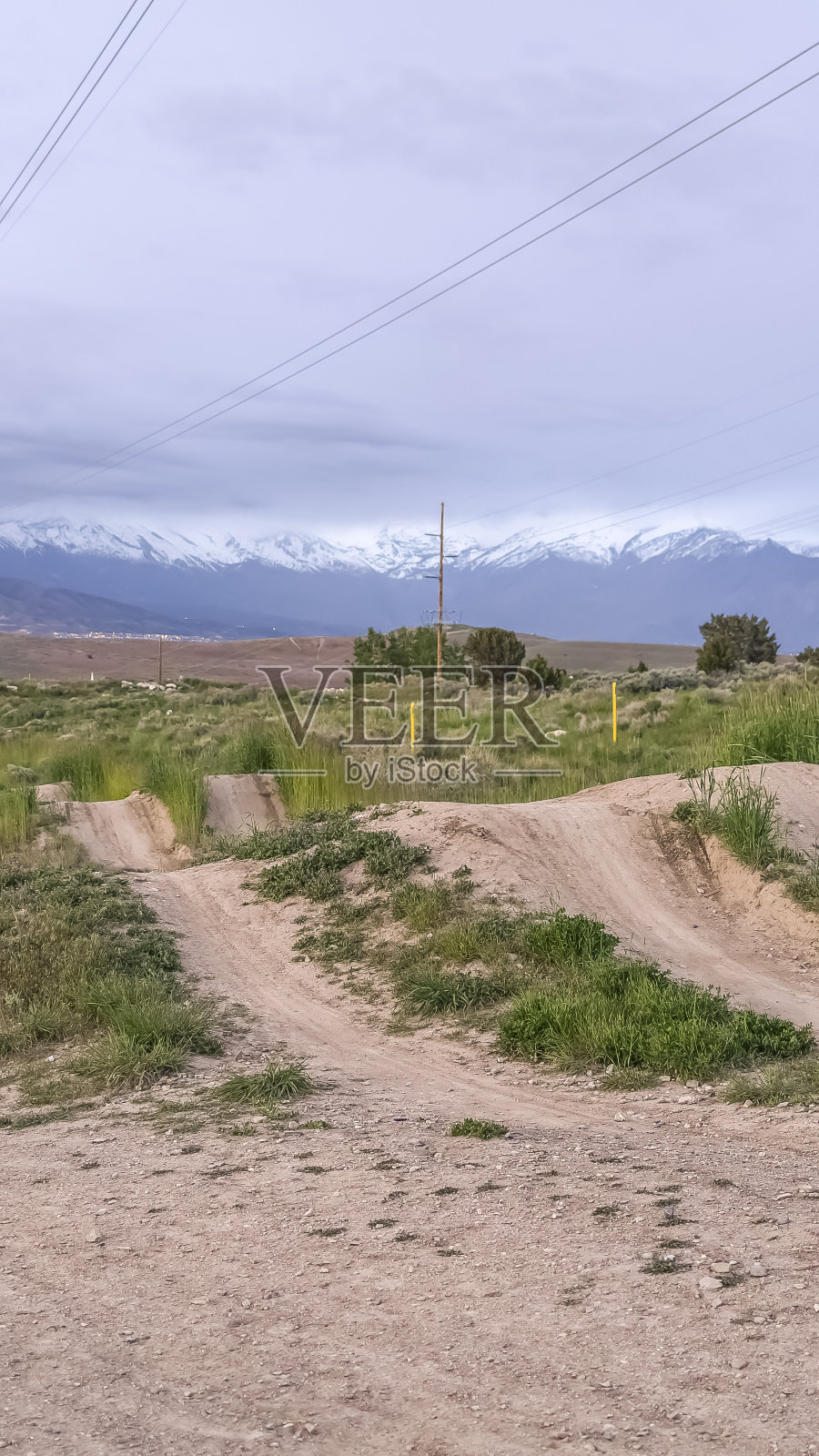垂直框架土路和草地与远处的雪山与多云的天空照片摄影图片