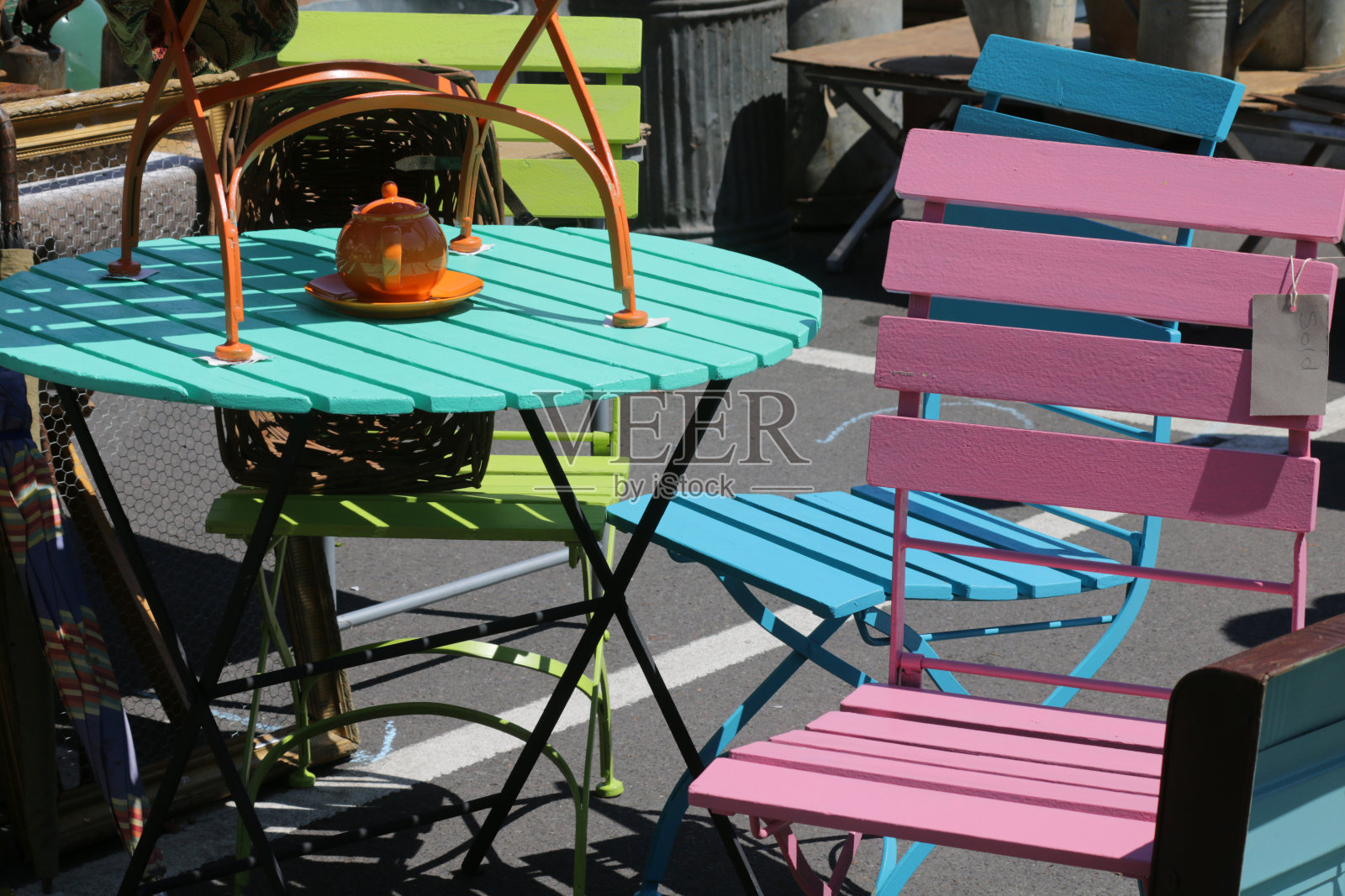 彩色的图像，圆形的金属和木制的花园庭院桌子和椅子，颜色鲜艳的彩虹漆，橙色，粉色，石灰绿，蓝色和绿松石，在园艺市场的摊位上出售，橙色的茶壶在外面用餐照片摄影图片