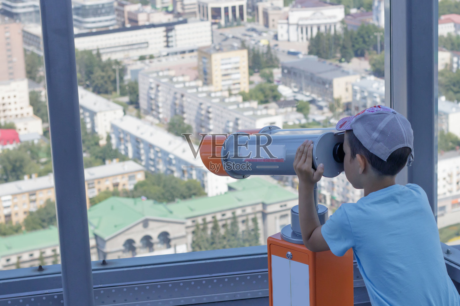 这个男孩从叶卡捷琳堡一座高层建筑的全景窗口通过望远镜往里看。照片摄影图片