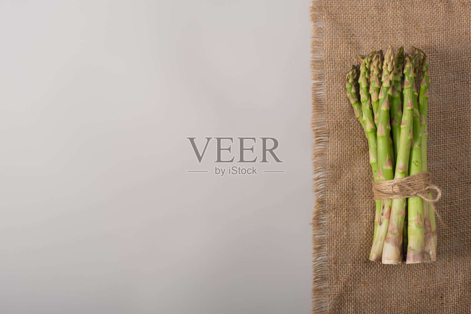 顶视图一束绿色芦笋用绳子绑在麻袋上，在灰色的背景上照片摄影图片