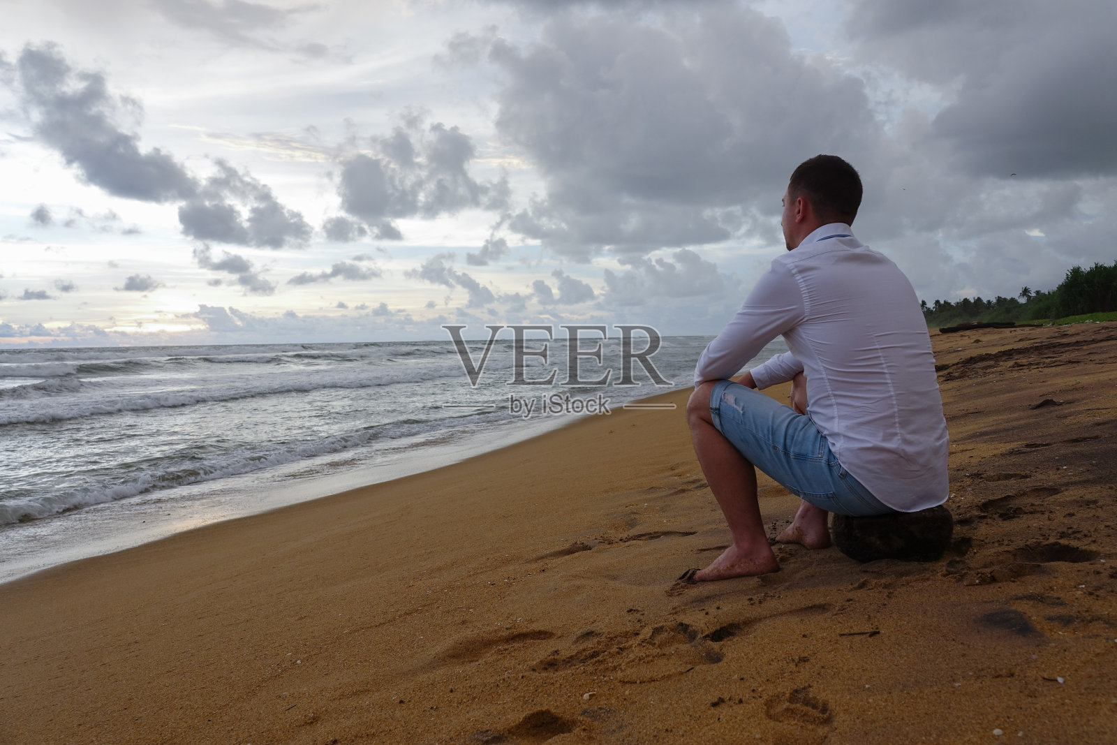 在热带海滩上迎接日落的白衬衫年轻男人照片摄影图片