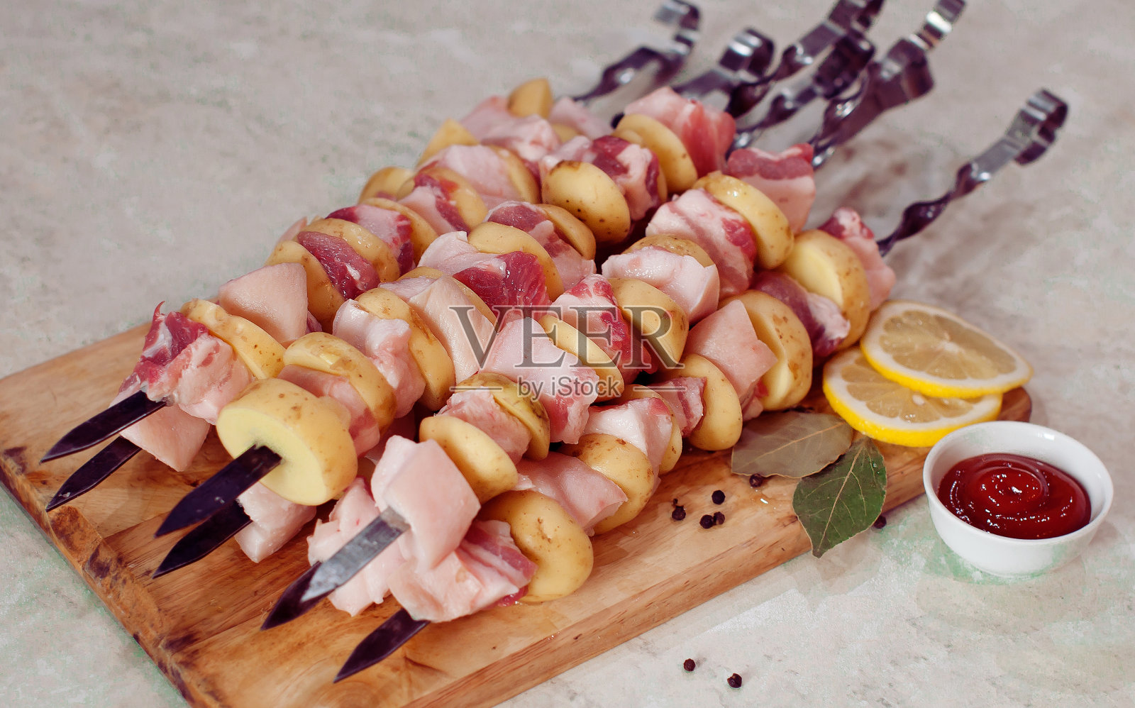 肥美的生猪肉和土豆串在烤肉串上，烧烤时用柠檬和酱汁放在砧板上照片摄影图片