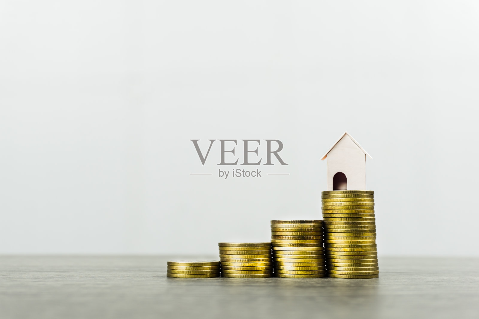 房地产投资的概念。存钱买新房子。房屋贷款,抵押贷款。在白色的背景和空间衬托下，一堆硬币放在木桌上的小房子模型。照片摄影图片