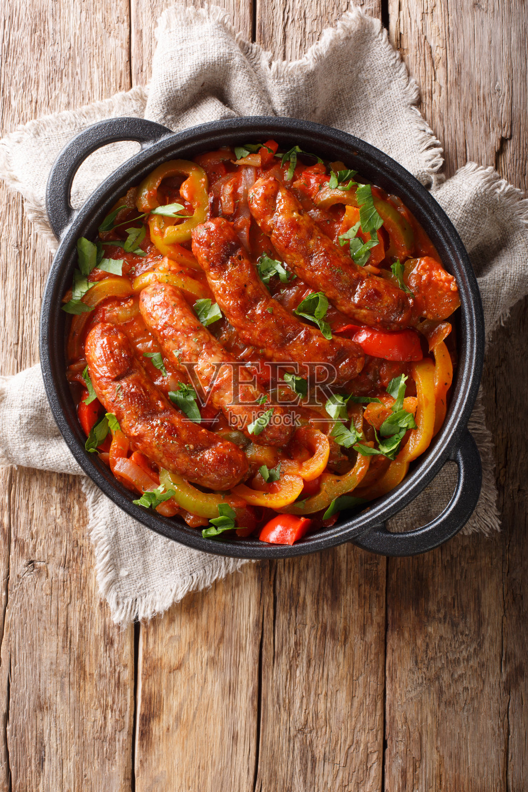 意大利食物烤香肠与烤辣椒，洋葱，香草和西红柿在煎锅中特写。垂直的俯视图照片摄影图片
