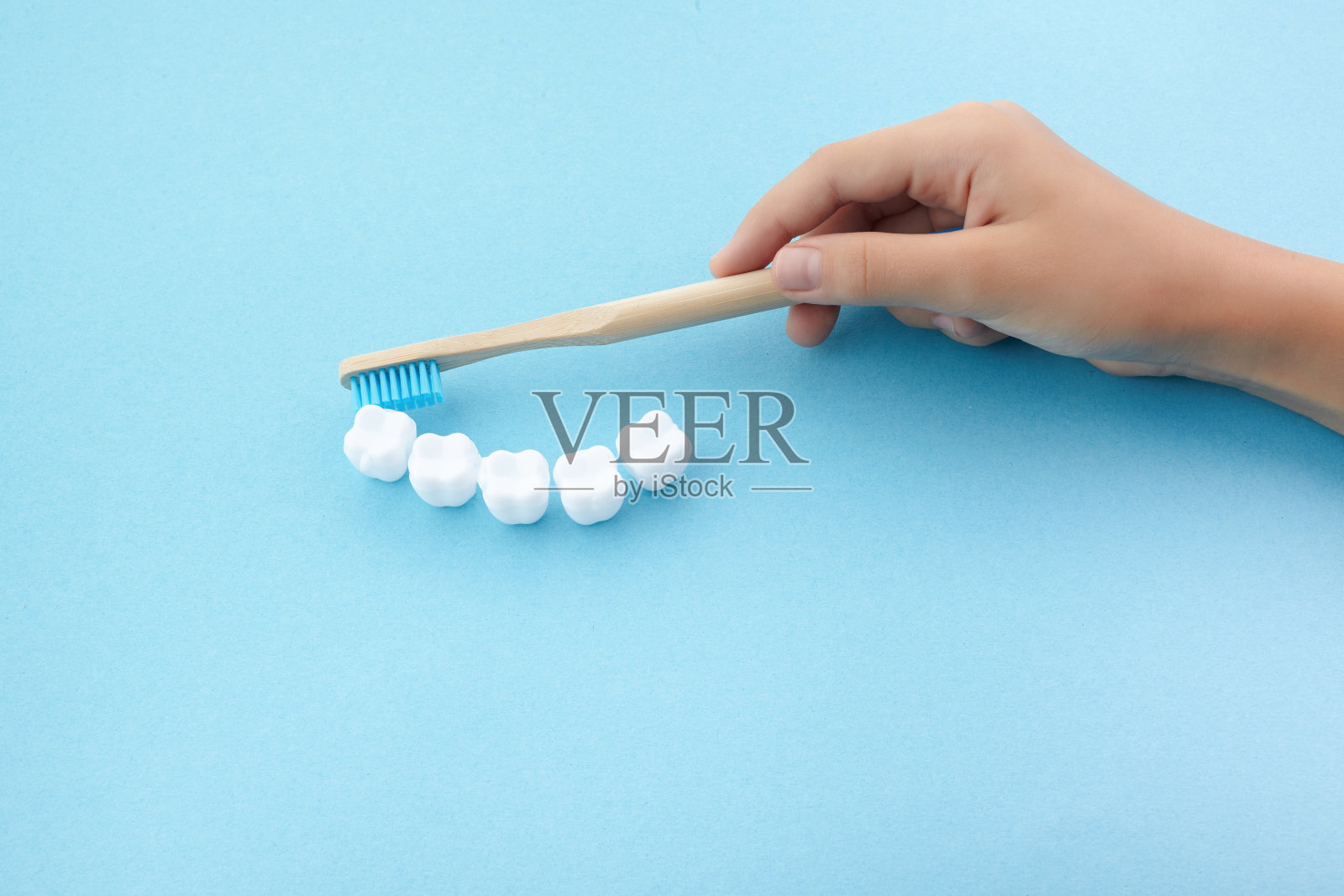 孩子的手与牙刷和白色塑料牙齿在蓝色背景照片摄影图片