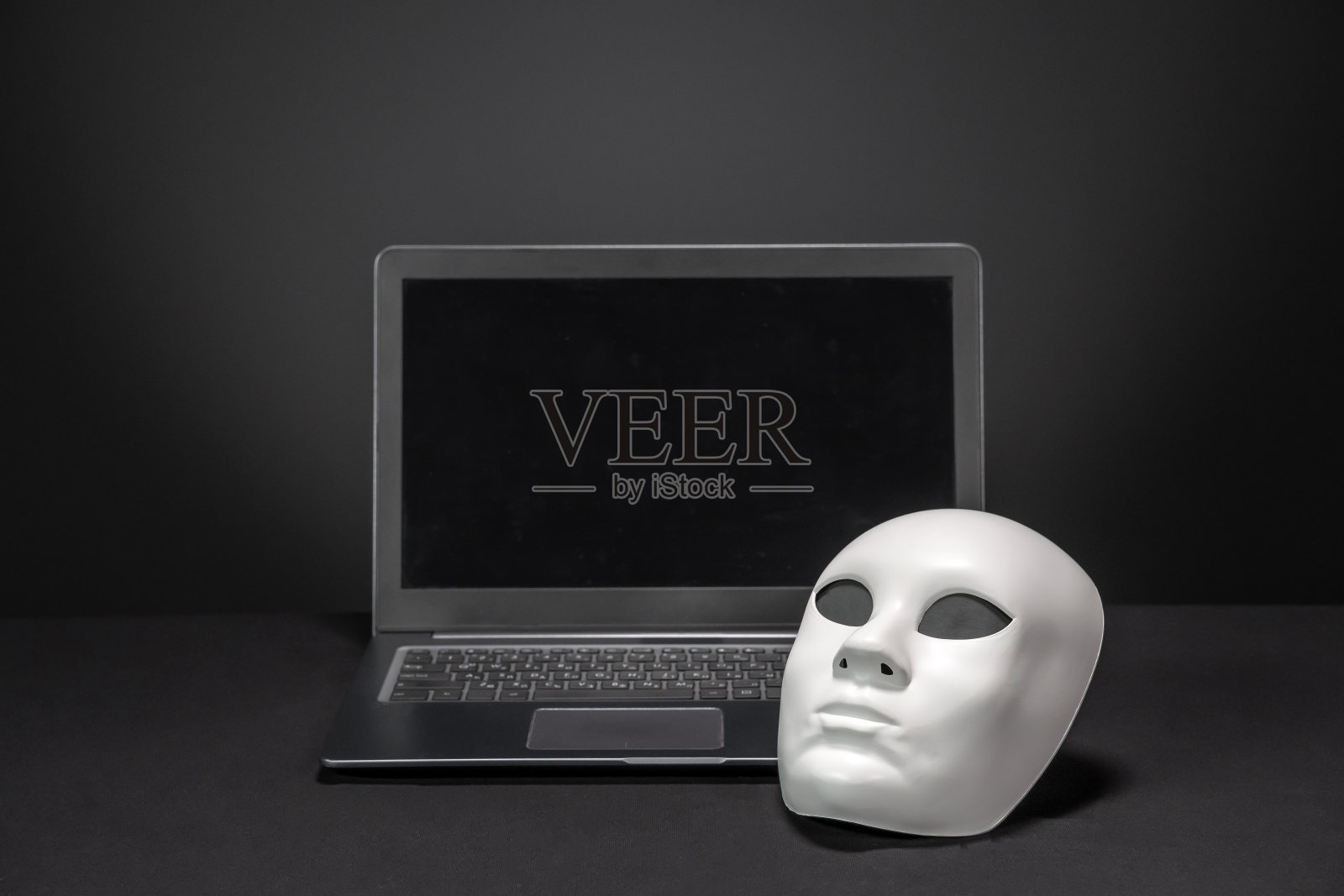 白色匿名面具旁边打开的笔记本电脑照片摄影图片