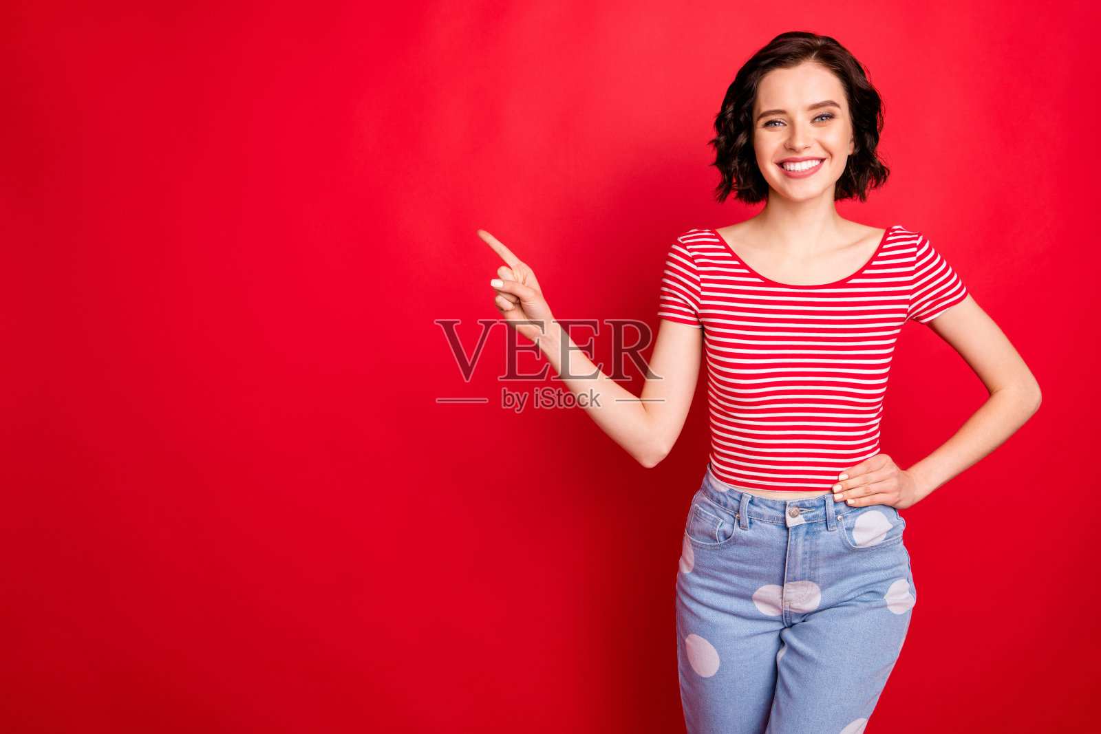 欢快的女孩指着空旷的空间，好像在说这一定是你的广告，而孤立的红色背景照片摄影图片