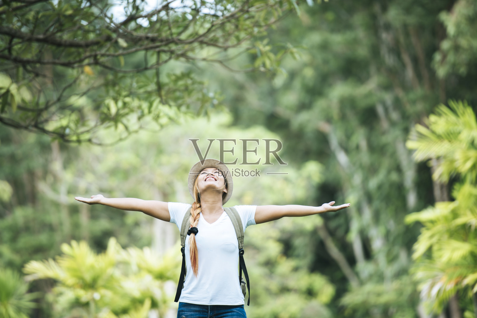 年轻幸福的女子背着双肩包举起手，与大自然一起享受。女性旅游的概念。照片摄影图片