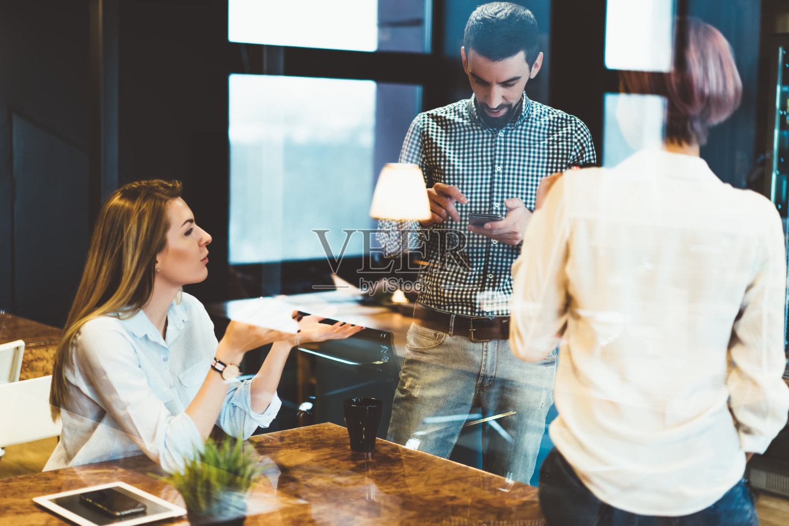 专业设计师团队相互沟通，使用智能手机设备站在办公室内部的玻璃墙。青年讨论共同项目合作计划照片摄影图片