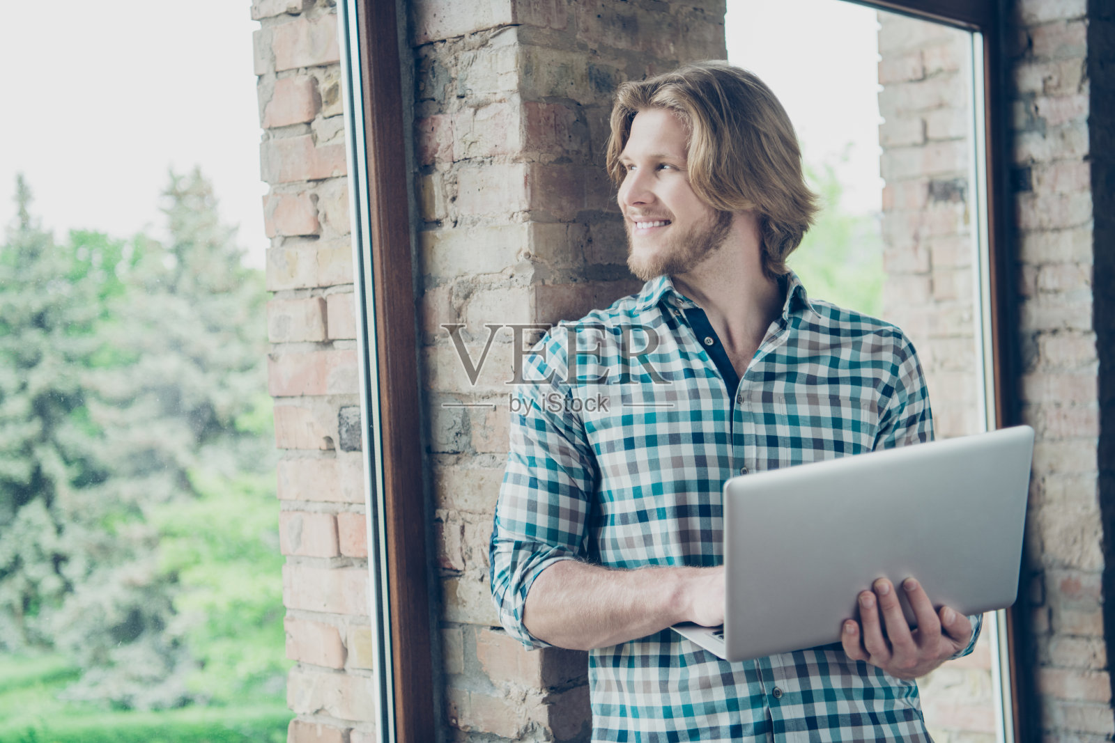室内穿着格子衬衫的金发握着装置的轻松人的侧面照片照片摄影图片