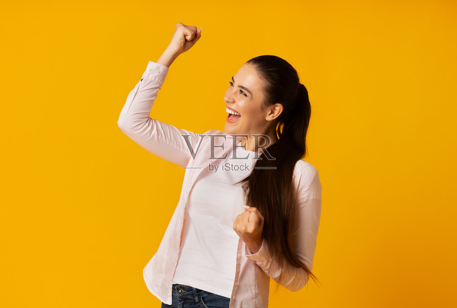 漂亮的黑发女孩摇动拳头庆祝成功在黄色背景照片摄影图片