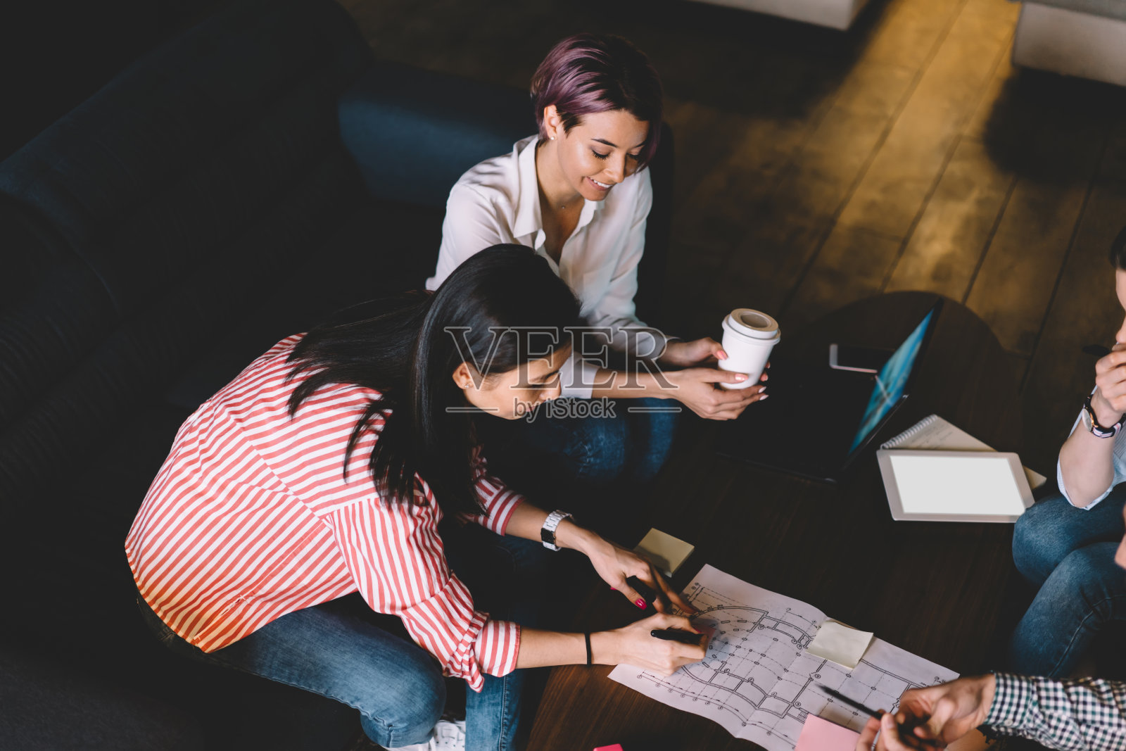 成功的同事们合作绘制建筑项目的平面方案并讨论想法，在共同工作的办公室里，专业的设计师们一起坐在桌子上创作草图照片摄影图片