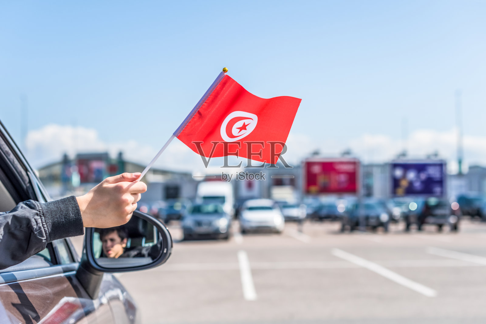 一个男孩拿着突尼斯国旗从打开的车窗在购物中心的停车场。概念照片摄影图片