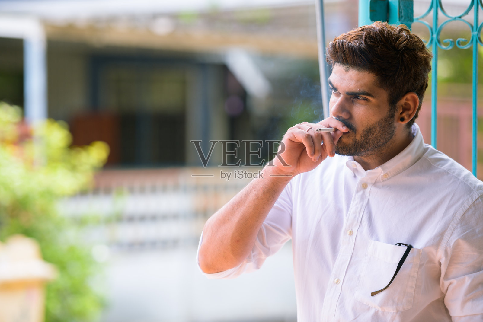 年轻英俊的留着胡子的印度男子在户外抽烟时思考照片摄影图片