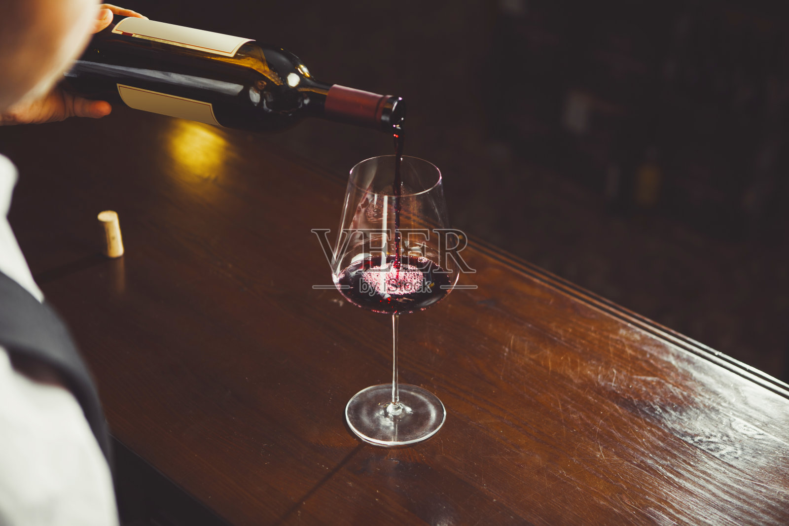 特写照片，侍酒师在吧台背景上倒红酒到杯子里。照片摄影图片