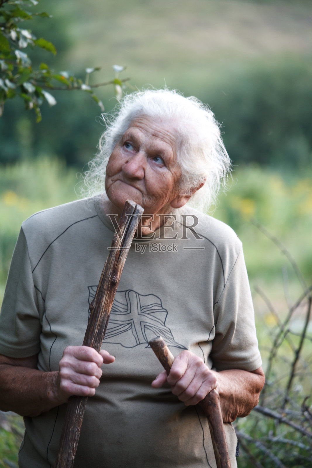 一位患有关节炎的老妇人拄着拐杖在草地上行走，选择性聚焦照片摄影图片