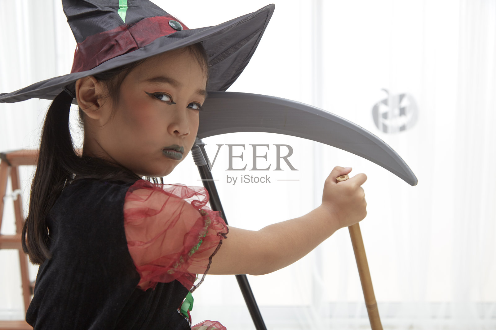 万圣节快乐。一个穿着女巫服装的漂亮小女孩用南瓜装饰着家里照片摄影图片