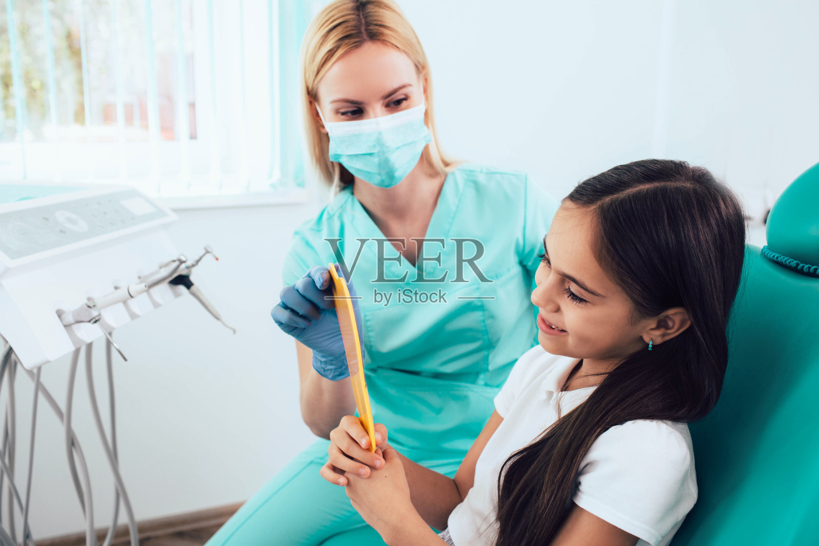 小女孩在牙科诊所牙齿治疗成功后，看着镜子微笑。小儿牙科照片摄影图片