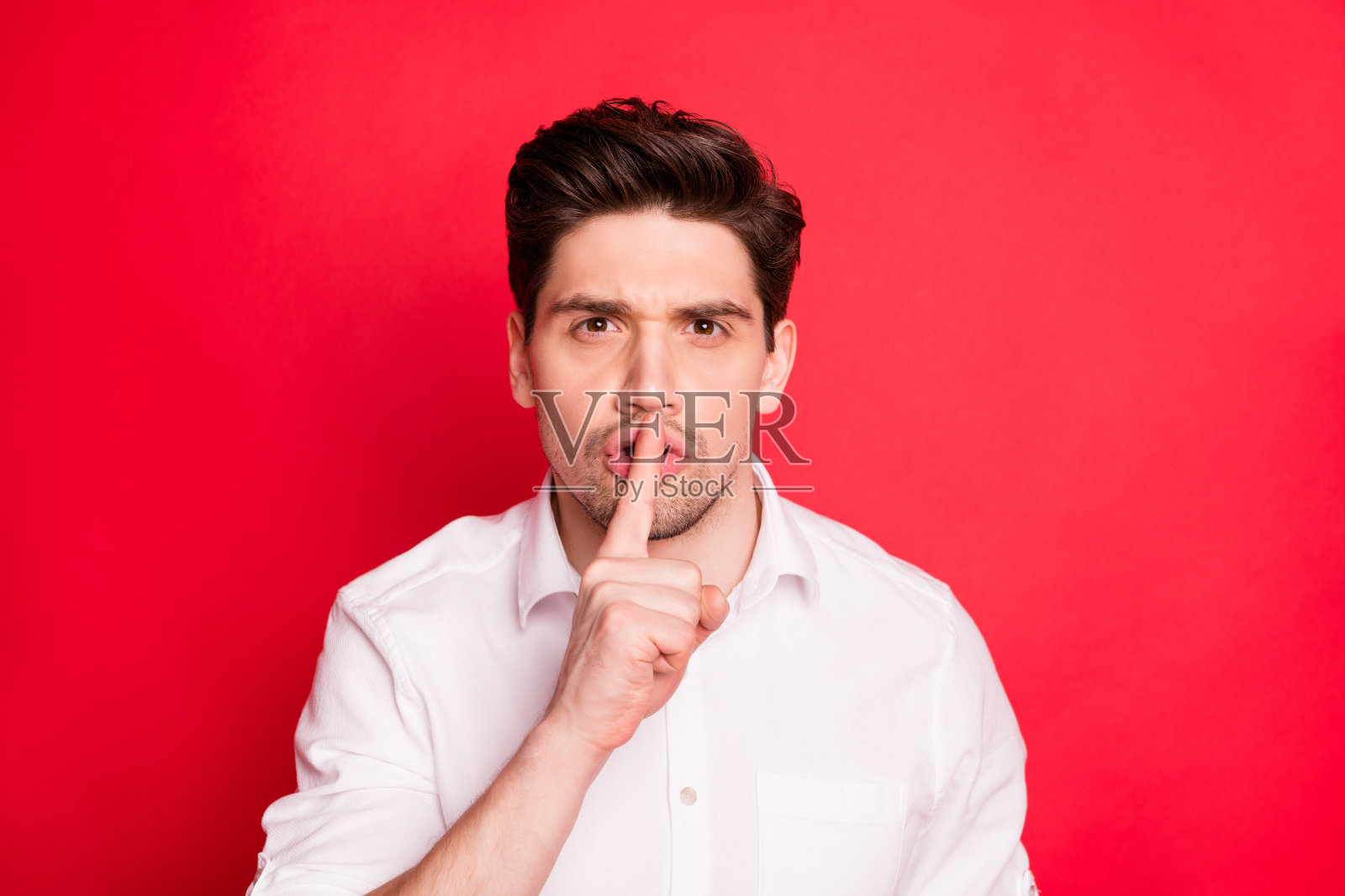 他的特写肖像，他漂亮的，有吸引力的，专注的，严肃的男人显示嘘标志，保持我的秘密孤立在明亮的，生动的，闪亮的红色背景照片摄影图片