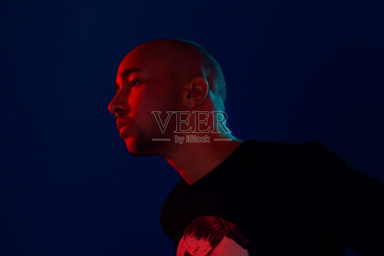 工作室拍摄的一个年轻的纹身光头男子在蓝色背景下摆姿势。90年代的风格照片摄影图片