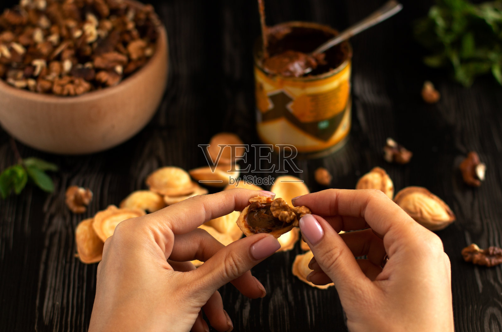 双手将坚果饼干与炼乳和坚果放在有绿色蔬菜的深色木桌上照片摄影图片