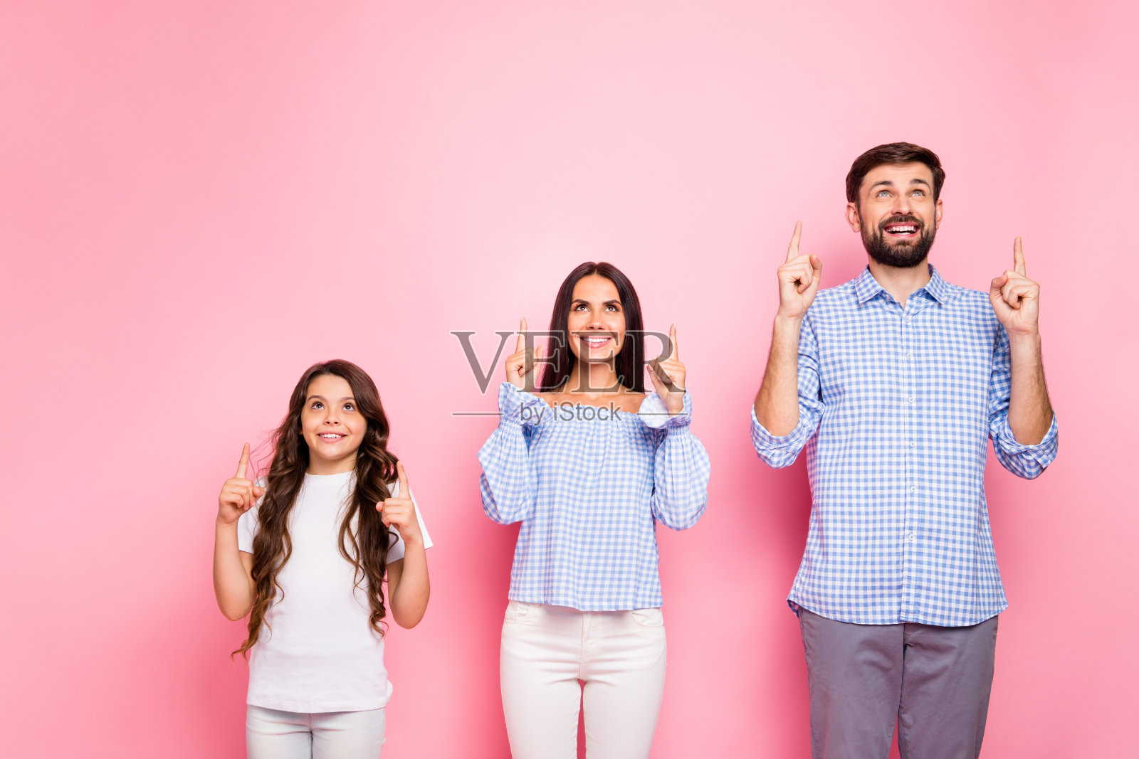 欢乐的家庭肖像与波浪长发型向上穿白色t恤长裤格子格子衬衫的肩膀孤立在粉红色的背景照片摄影图片