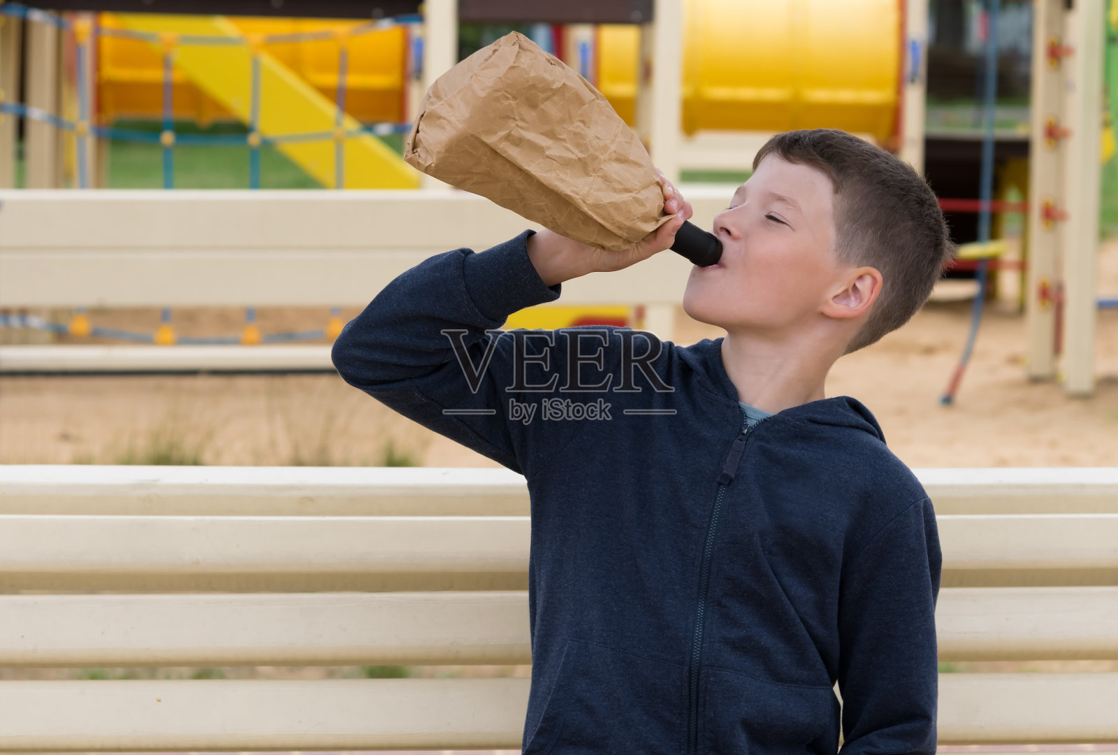 那男孩坐在长凳上用瓶子喝水照片摄影图片