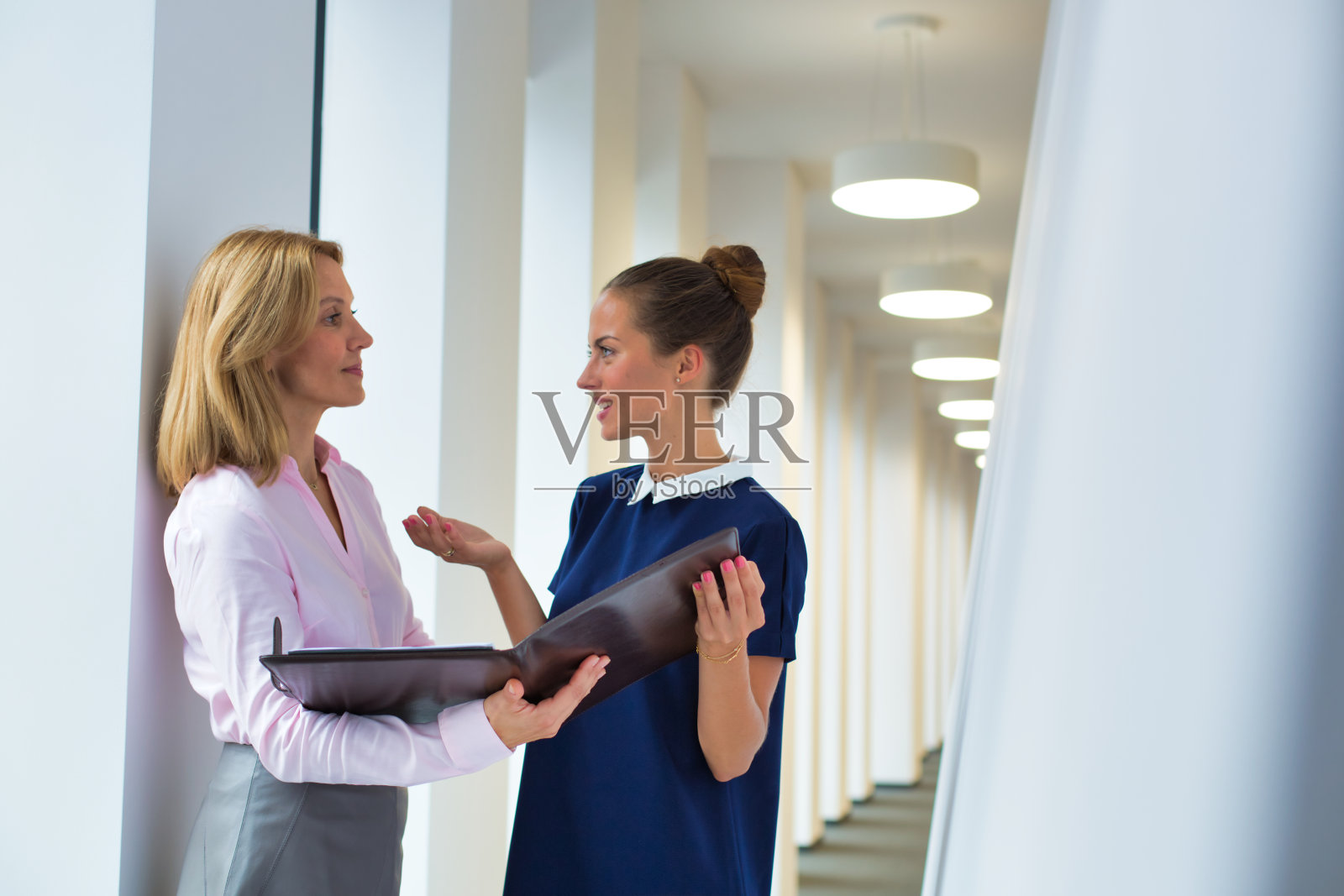 女商人站在办公室的走廊里讨论文件照片摄影图片