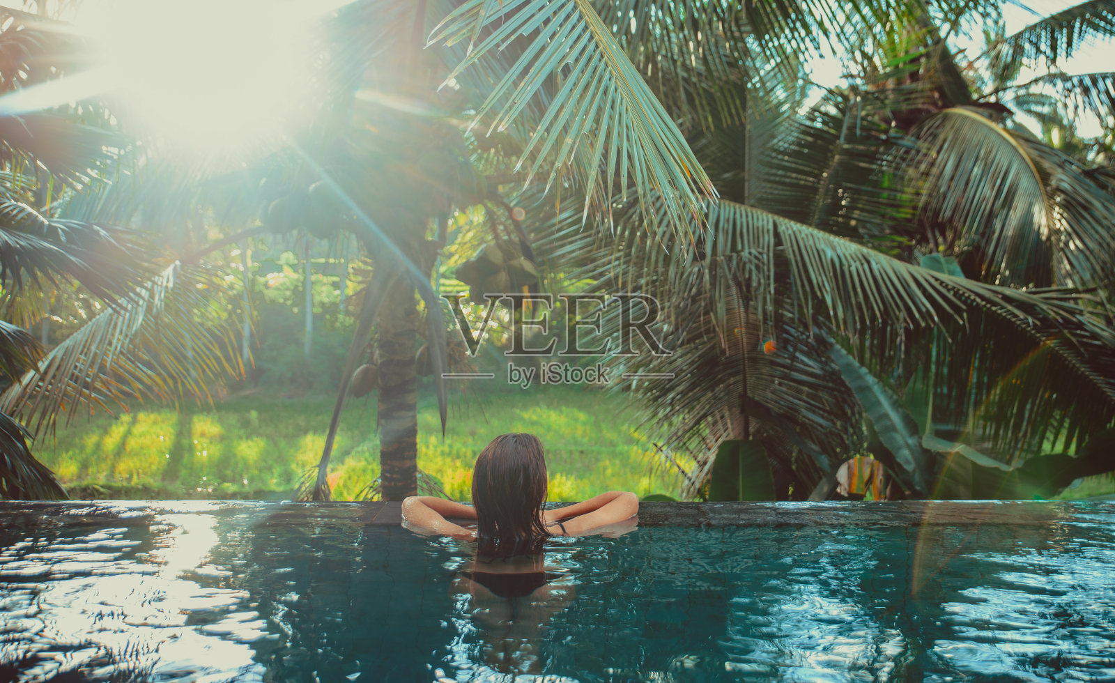 美丽的女孩放松在她的室外花园游泳池。夏季概念:生活方式、美容、度假和房地产照片摄影图片