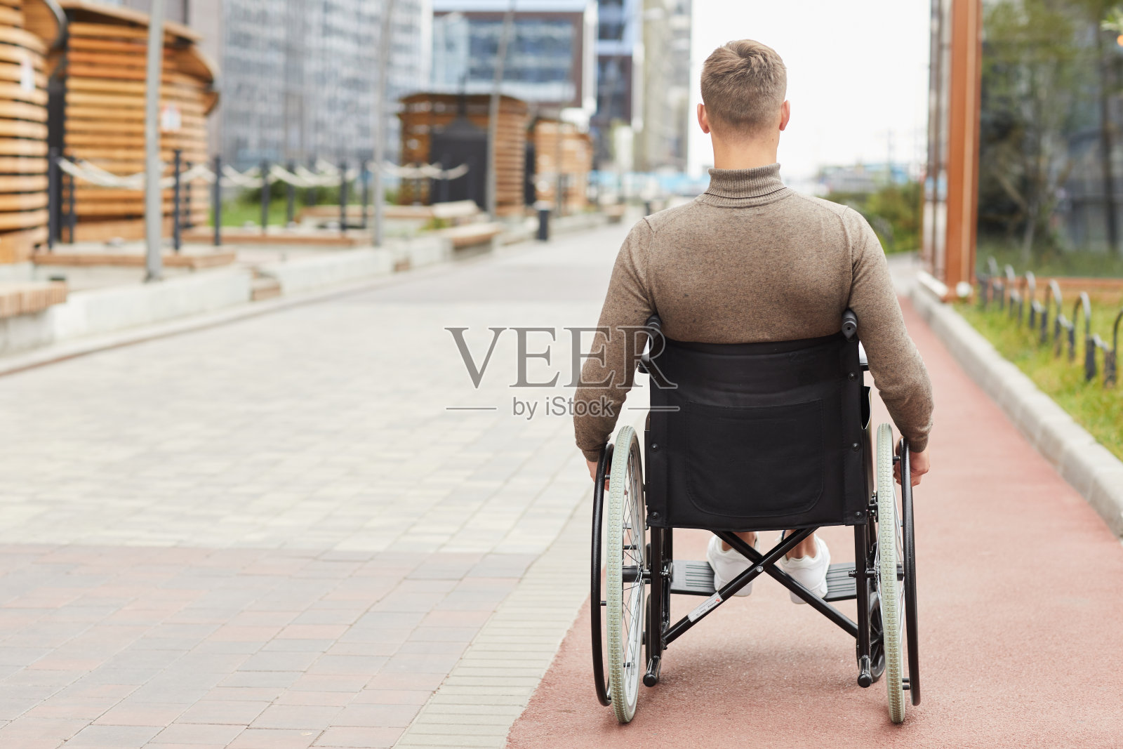 后视图的年轻人与身体残疾坐在轮椅和移动的城市街道照片摄影图片