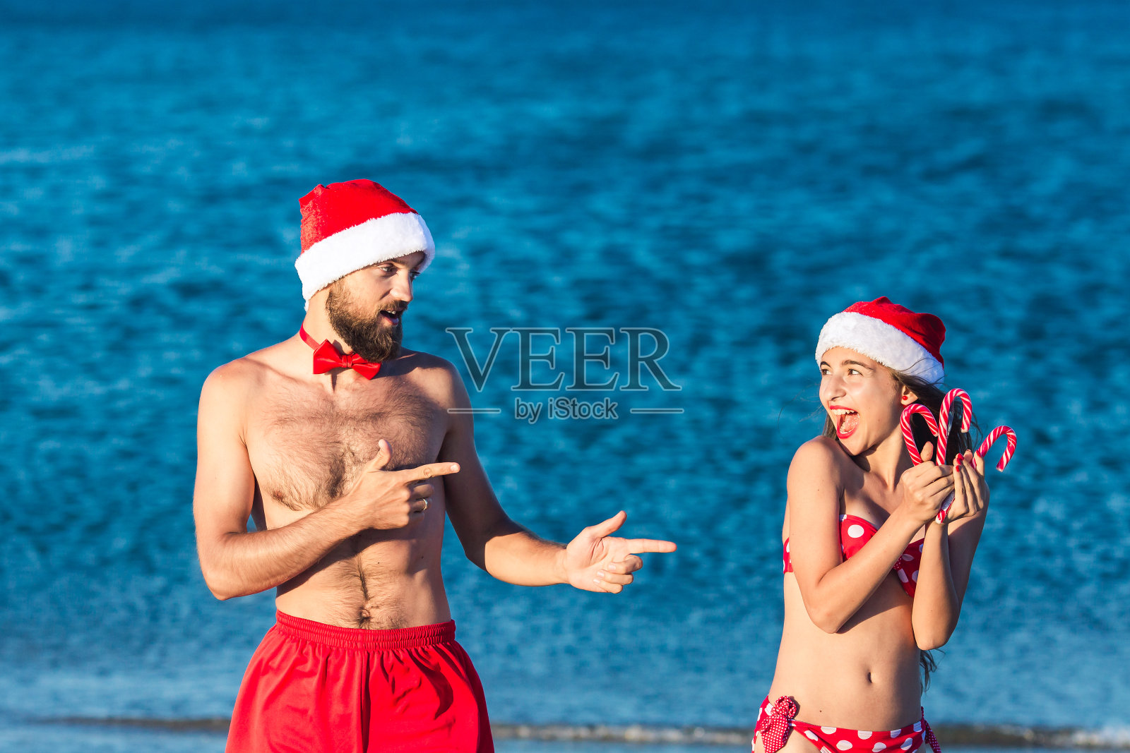 快乐的男人和女孩戴着圣诞帽拿着圣诞棒棒糖。照片摄影图片