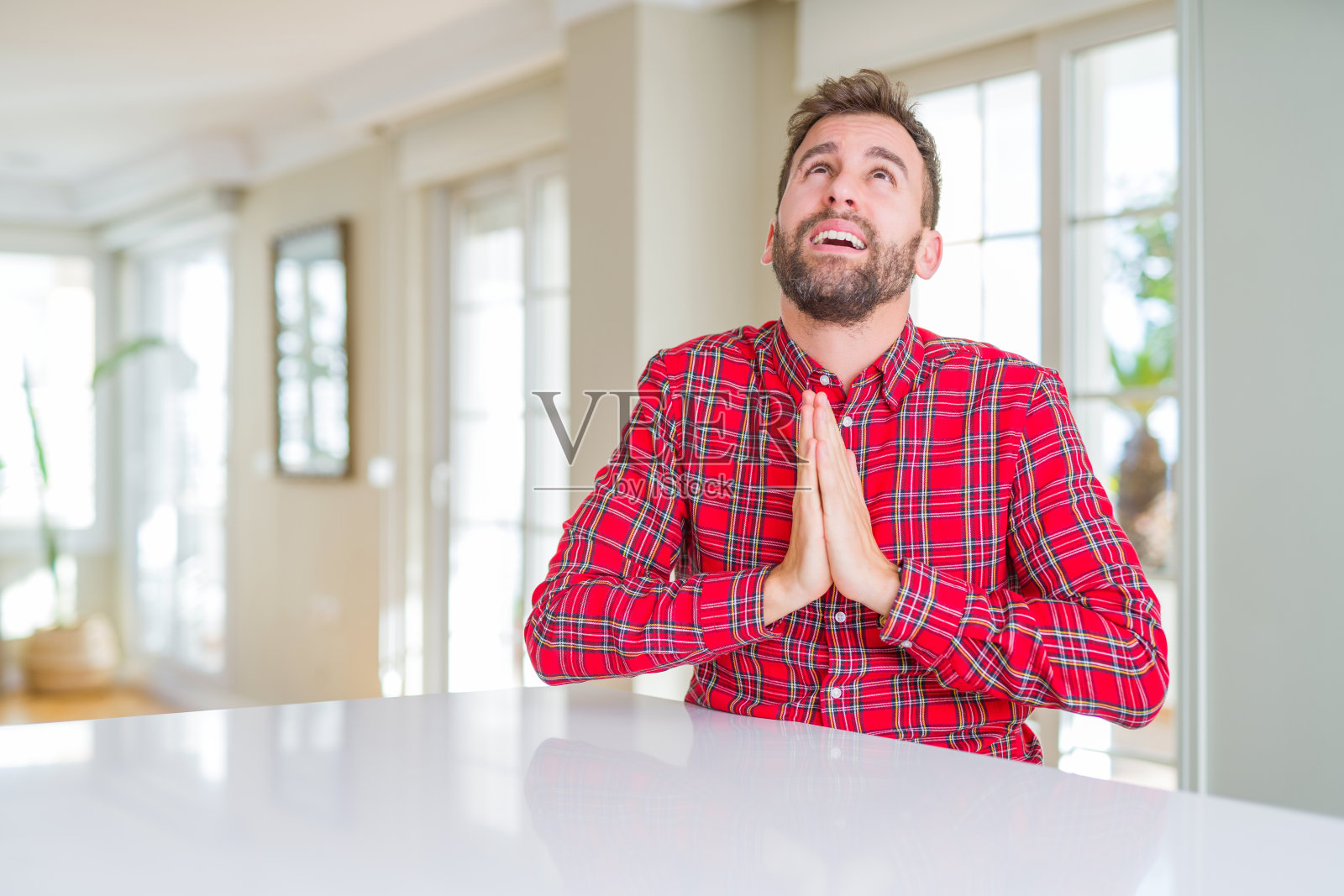 英俊的男子穿着五颜六色的衬衫，双手一起乞讨和祈祷，脸上带着希望的表情，非常情绪化和担心。请求宽恕。宗教的概念。照片摄影图片