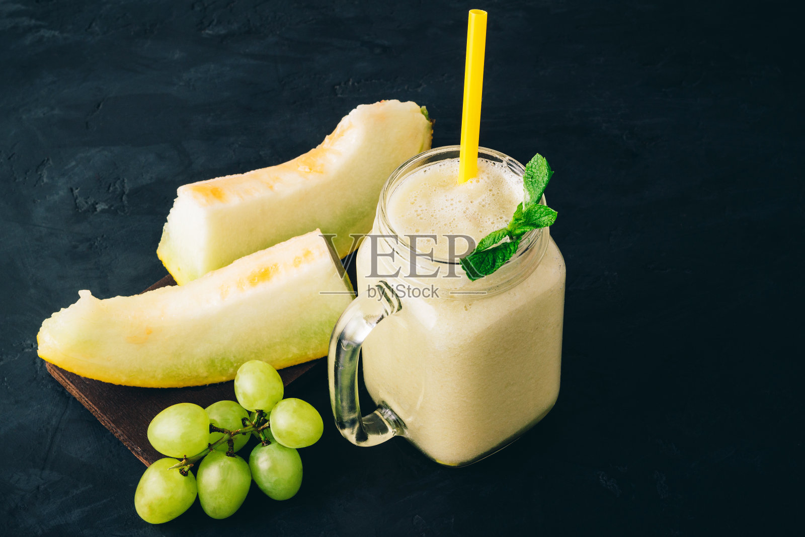 甜瓜冰沙在一个罐子与新鲜薄荷叶和葡萄在黑暗的背景照片摄影图片