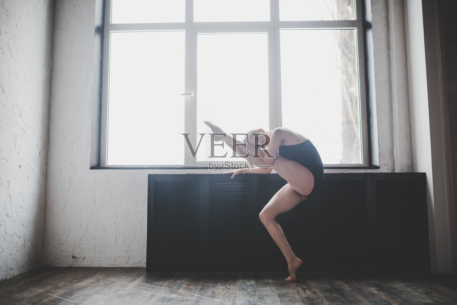 可塑性苗条的女人在窗前跳舞。专业舞者喜欢舞蹈。女舞者在课堂上训练现代芭蕾。当代舞蹈演员。日光下，剪影美丽的身躯。舞蹈的主题照片摄影图片